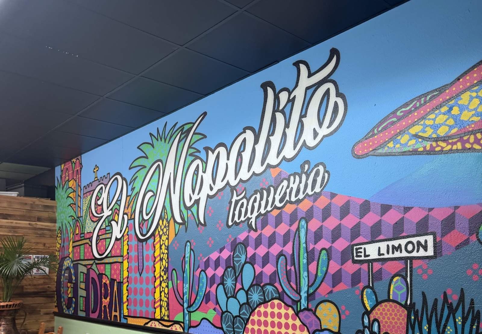 The El Nopalito dining room mural: script lettering over painted cacti, a pink cube pattern and a sky-blue wall